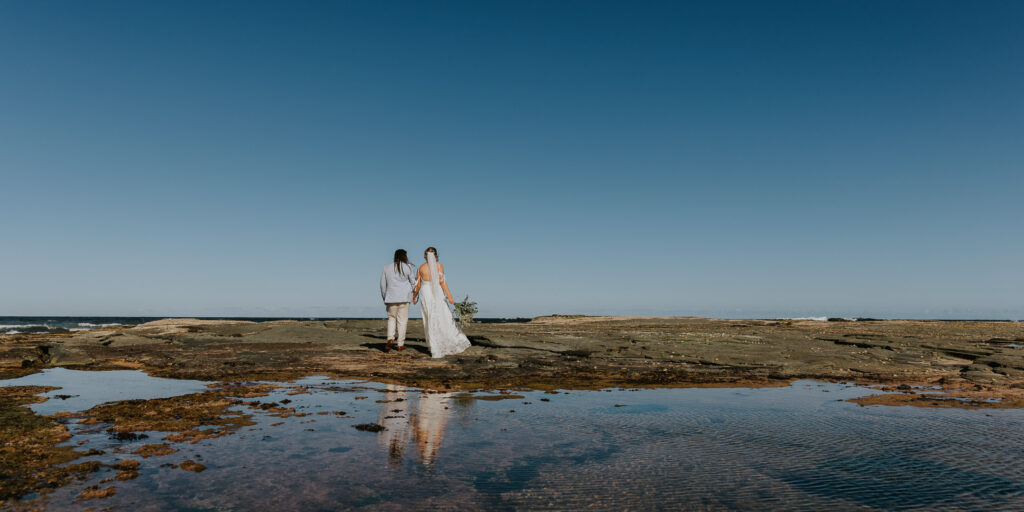 Couple walking on a rockeries with water on under a blue sky