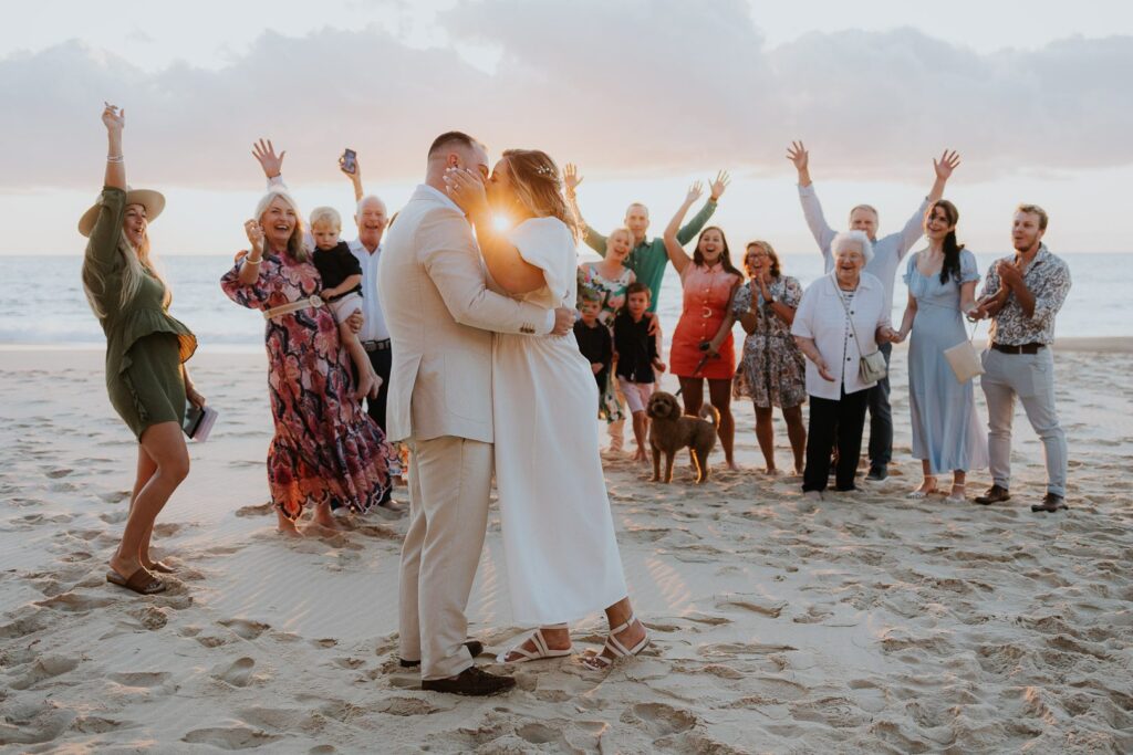 Sunrise Beach Elopement with a small group of family celebrating behind the kissing couple