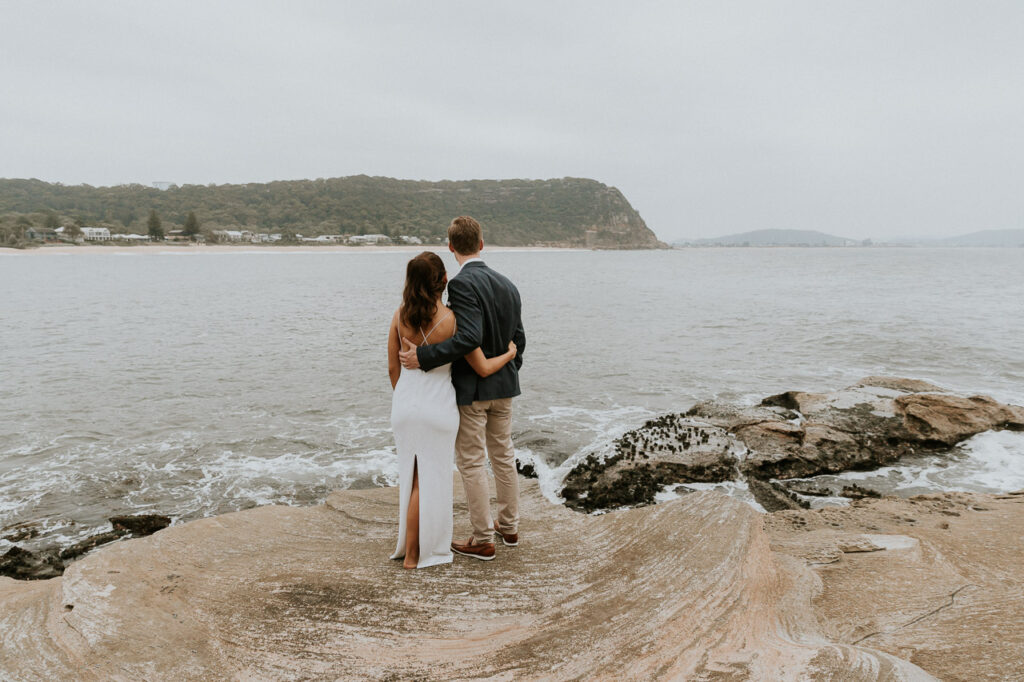 Pearl Beach on the Central Coast Elopement photography and planning. A couple stand on the rocks and look out to the ocean